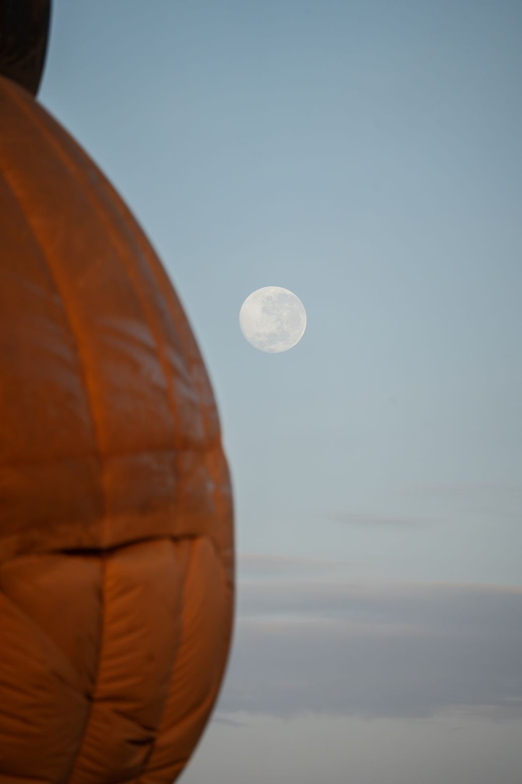 A hot-air balloon filling at dawn under a setting moon